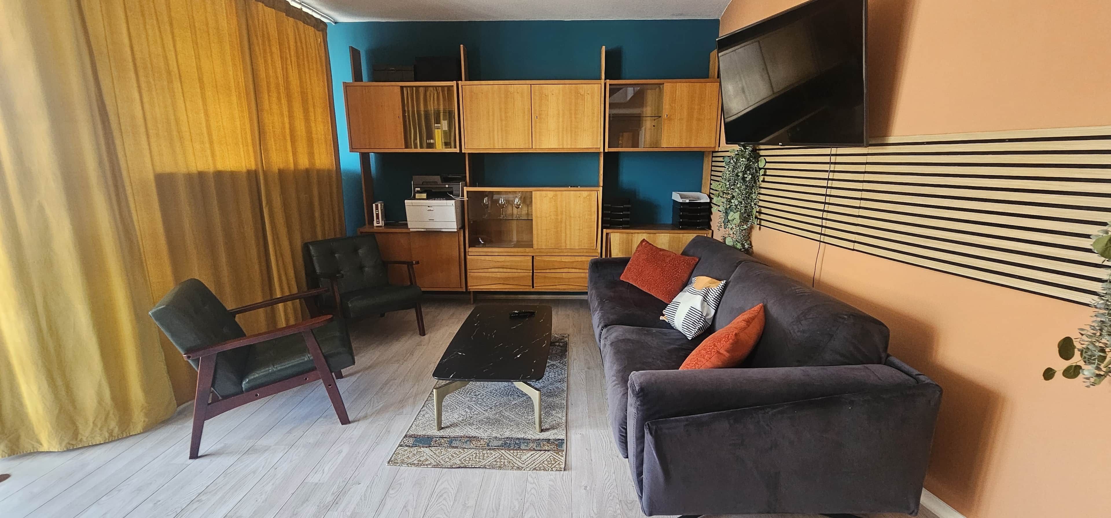 A living room with a sofa, chairs, a coffee table, and a TV mounted on the wall.