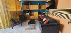 Un saló amb un sofà, cadires, una taula de centre i un televisor fixat a la paret.