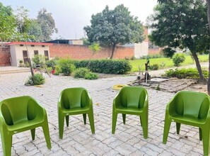 Un espacio exterior pavimentado con cuatro sillas de plástico verde dispuestas en fila.