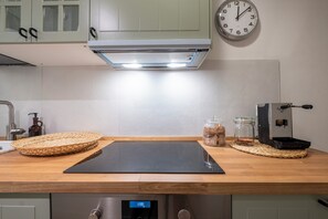 A kitchen with a black induction cooktop, a stainless steel range hood, a clock, and a coffee machine. - La Sera dei Miracoli by Wonderful Italy (Bologna)