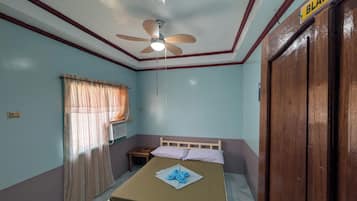 A bedroom with a bed, a ceiling fan, a window with curtains, a wooden door, and a 'BLAISE' sign.