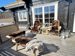 A wooden deck with outdoor furniture, including chairs and a bench, and a table with a glass top.
