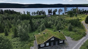 A house with a grass roof surrounded by dense forest, near a lake with a clear sky.