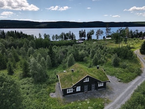 A house with a grass roof surrounded by dense forest, near a lake with a clear sky.