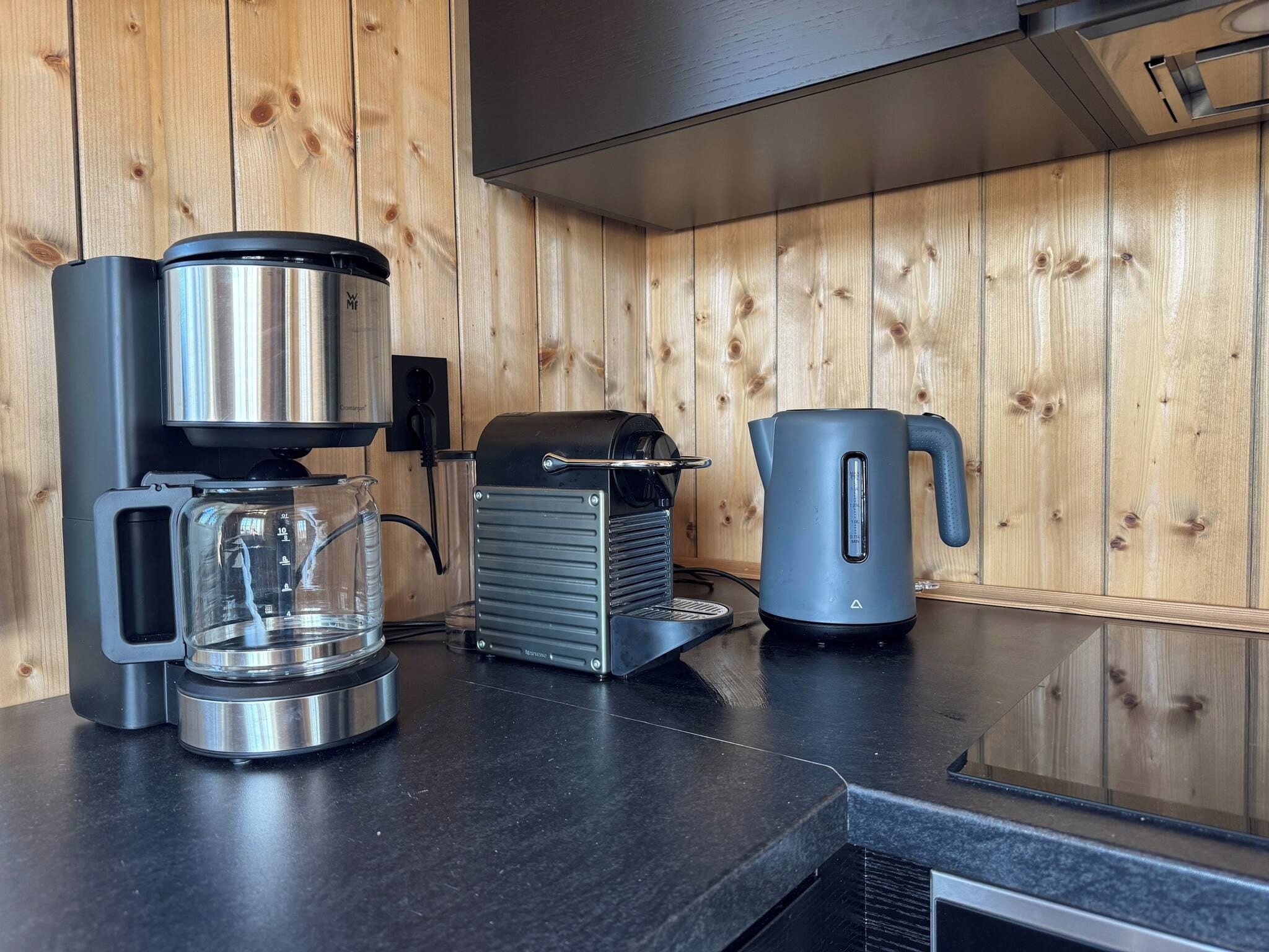 Una cocina con cafetera, hervidor y tostadora sobre una encimera negra.