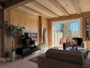 A living room with a television, sofa, and a large window with flags. - Familycabin at a Lake (Ringsaker)