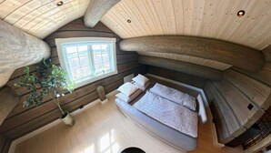 A high-ceilinged room with a large window, a bed with pillows, and a hanging plant.