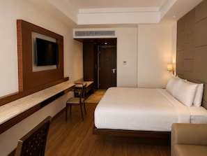A hotel room with a bed, a desk, a chair, a television, and a wall-mounted air conditioning unit.