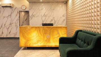 A reception area with a marble wall, a reception desk, a clock, and a green sofa.