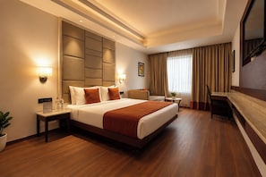 A hotel room with a large bed, a desk, a chair, a potted plant, and a TV.