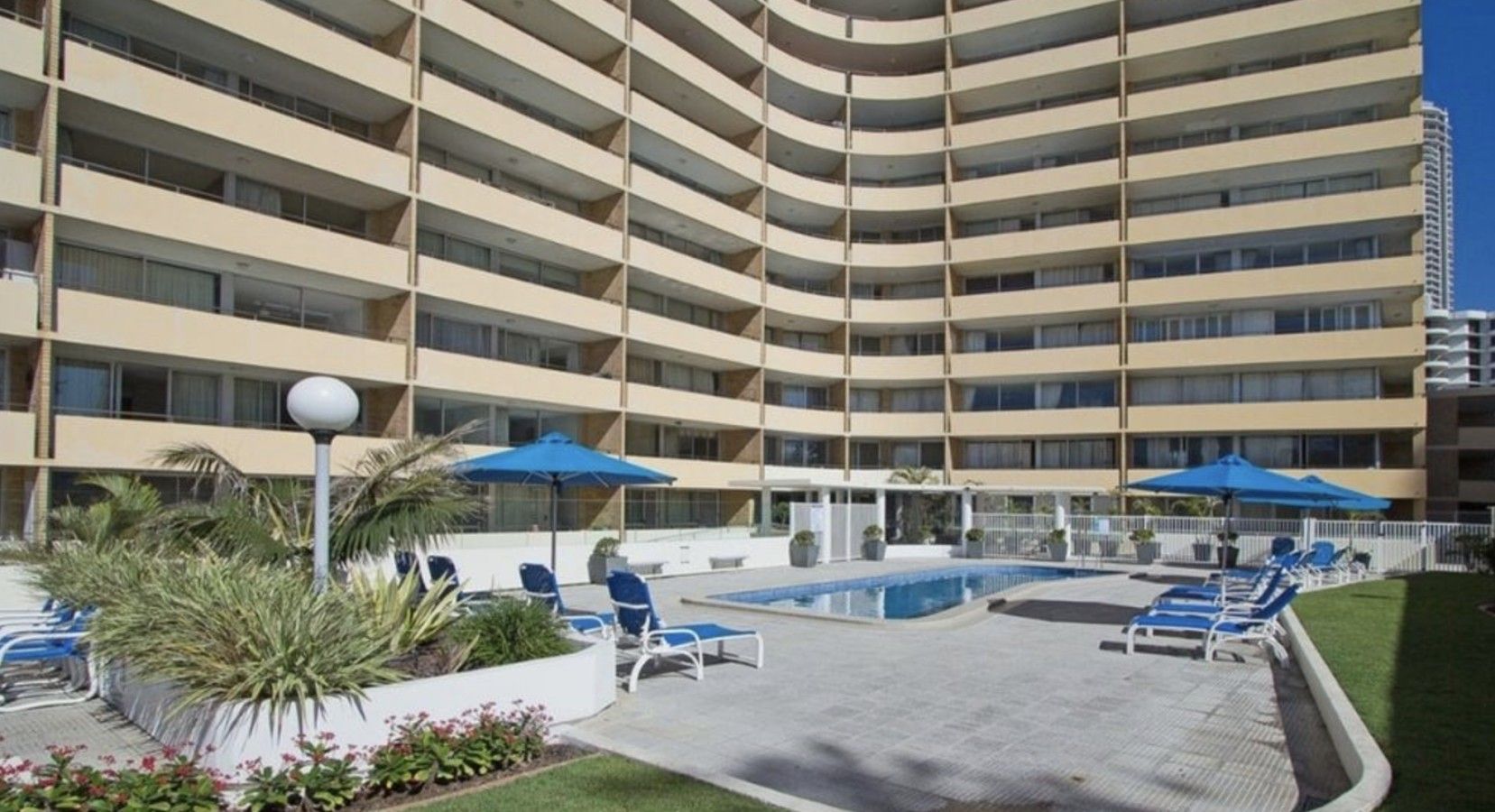A multi-story hotel with a pool area, lounge chairs, and umbrellas.
