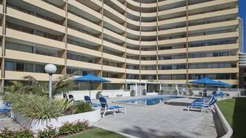 A multi-story hotel with a pool area, lounge chairs, and umbrellas.