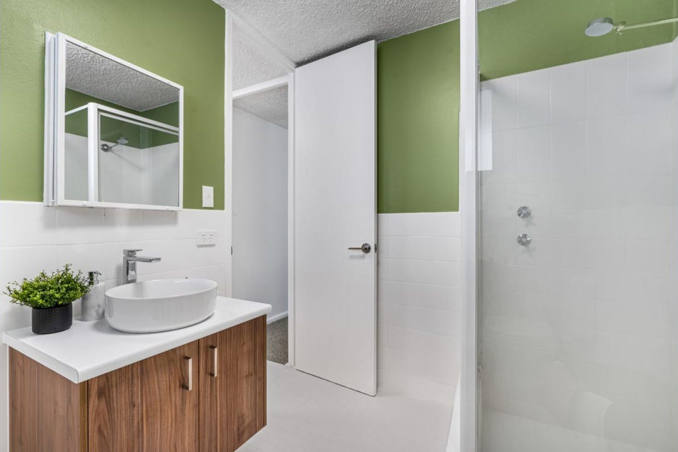 Een badkamer met een wit wastafel, een spiegel en een douchehoek.
