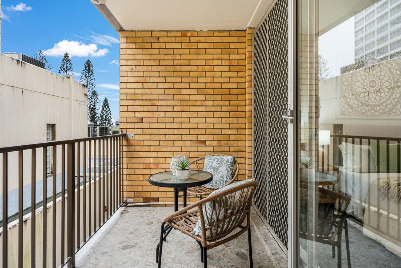 A balcony with a brick wall, a small table with a plant, and wicker furniture.