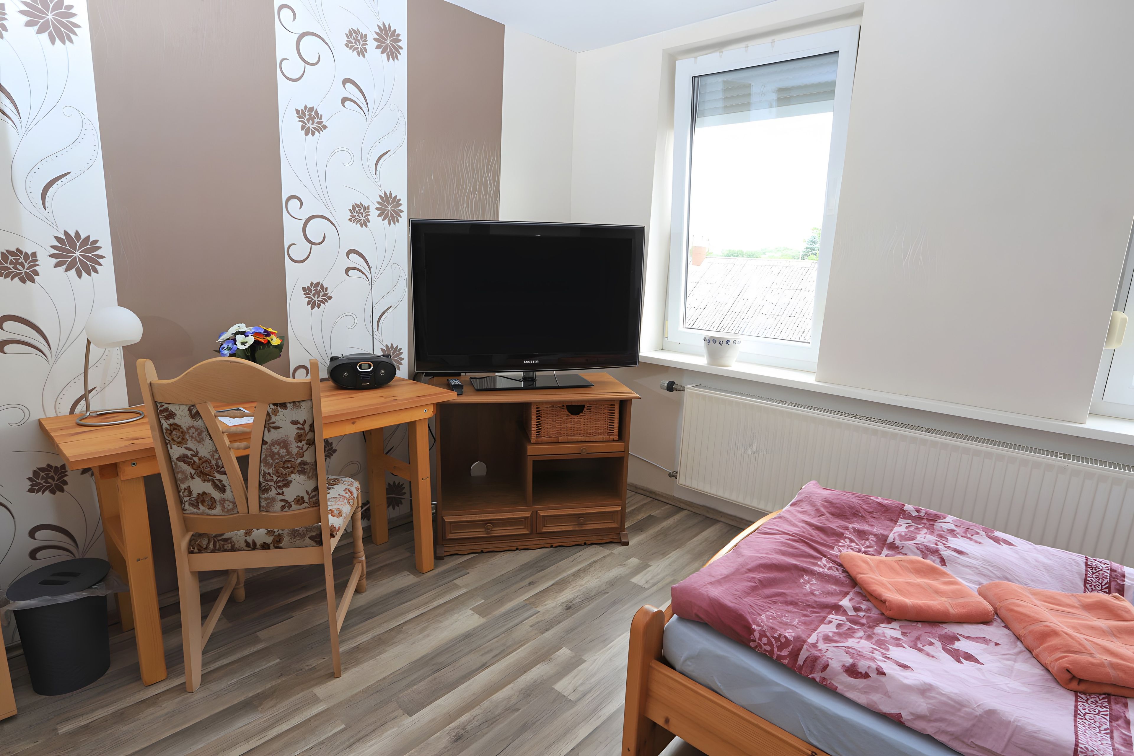 A room with a bed, a desk with a computer, a television, and a window.