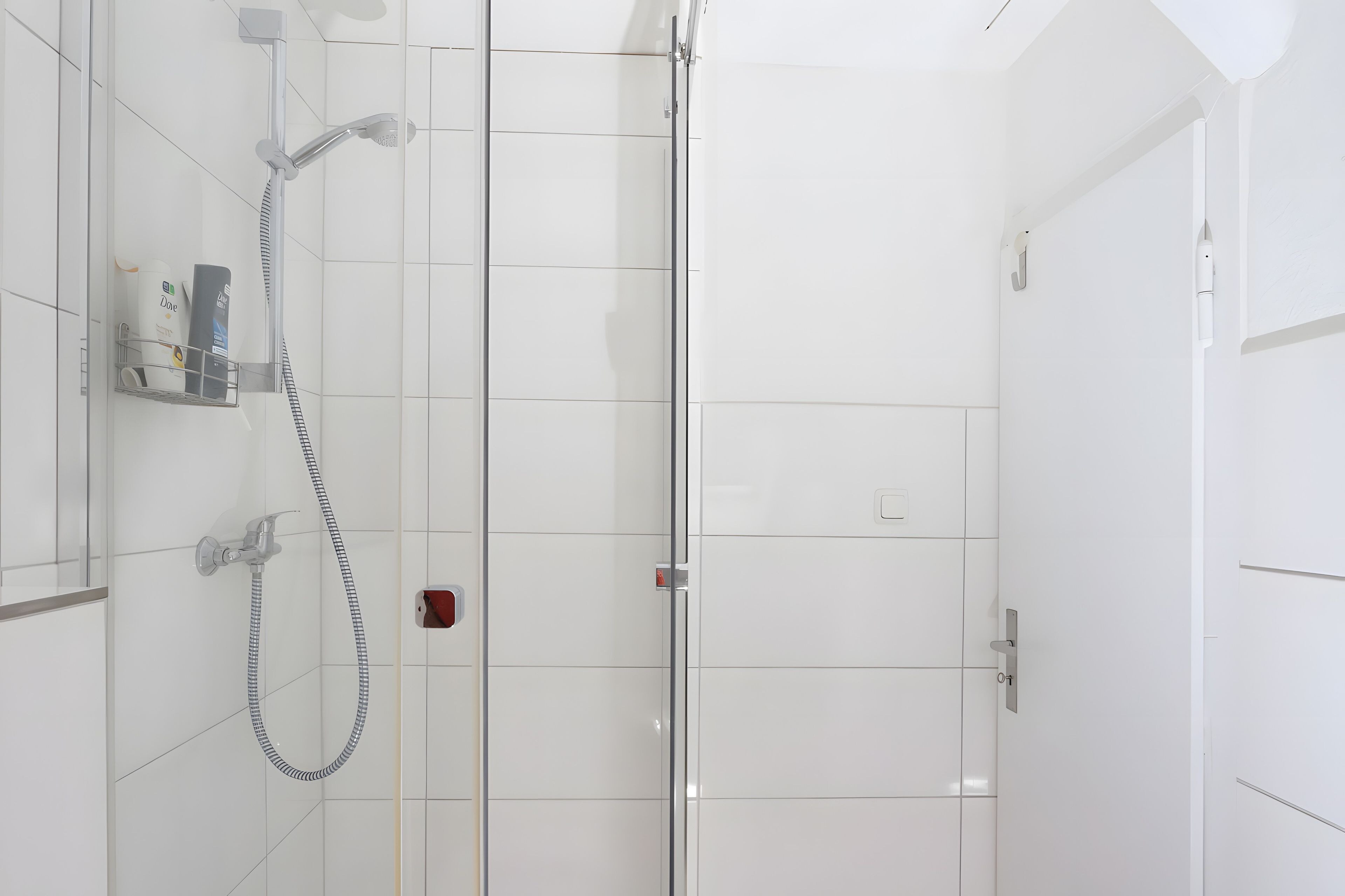 Ein modernes Badezimmer mit Duschkabine aus Glas, einer Handbrause und einem wandmontierten Wasserhahn.