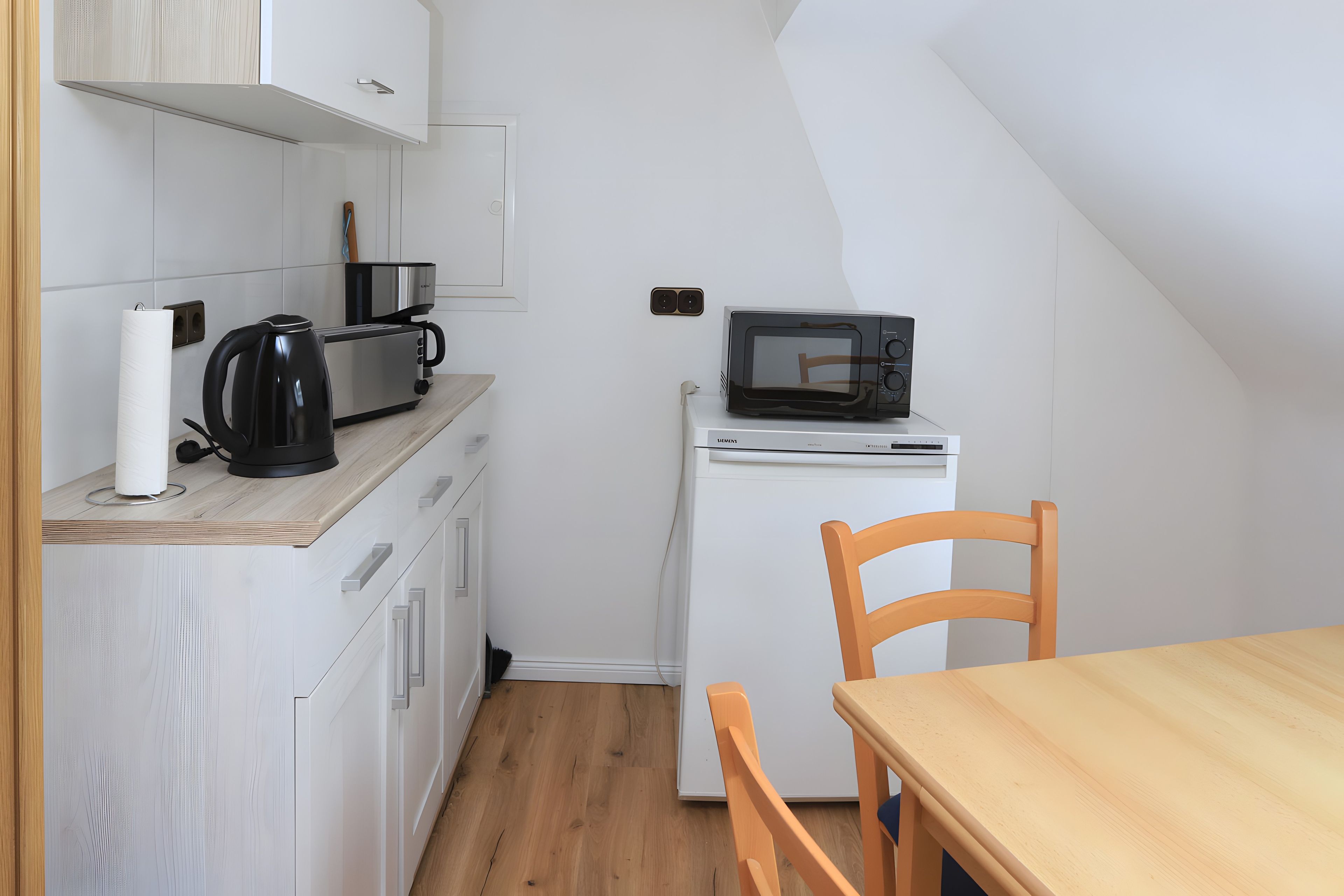 Eine kleine Küchenzeile mit Mikrowelle, Toaster und Wasserkocher auf einer weißen Arbeitsplatte.