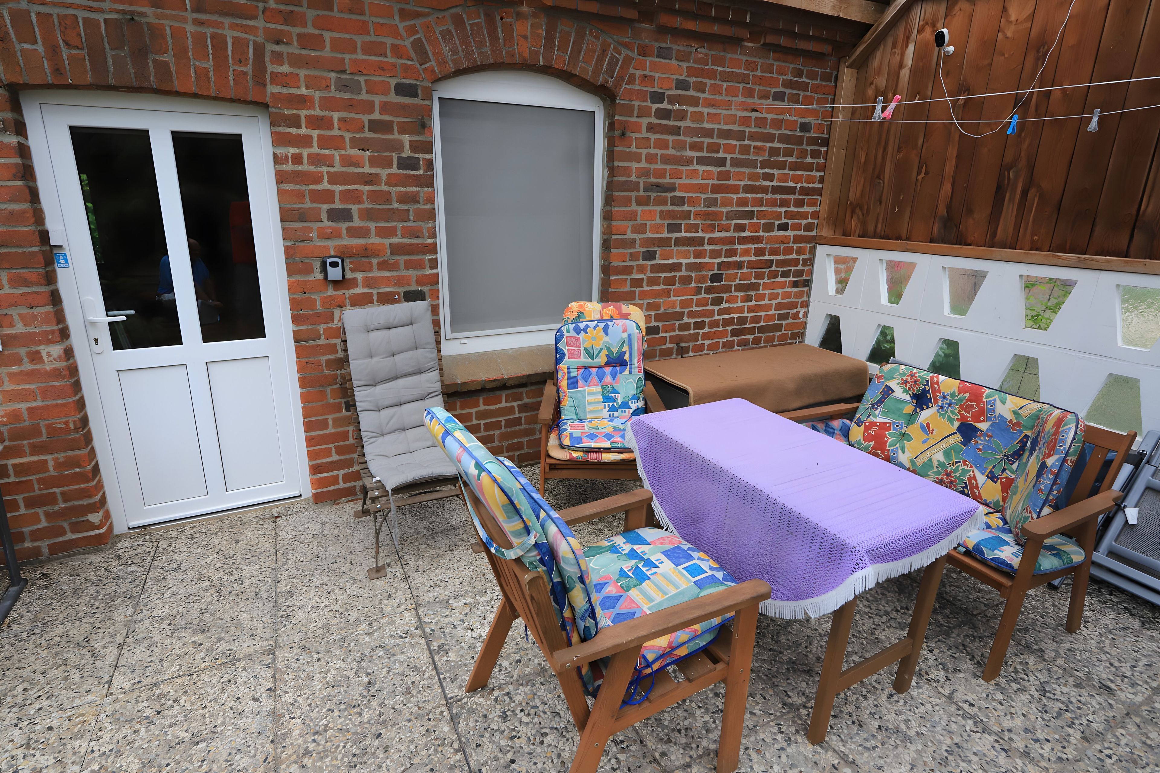Eine Terrasse mit Tisch und vier Stühlen, einer Tür und einer Ziegelwand.