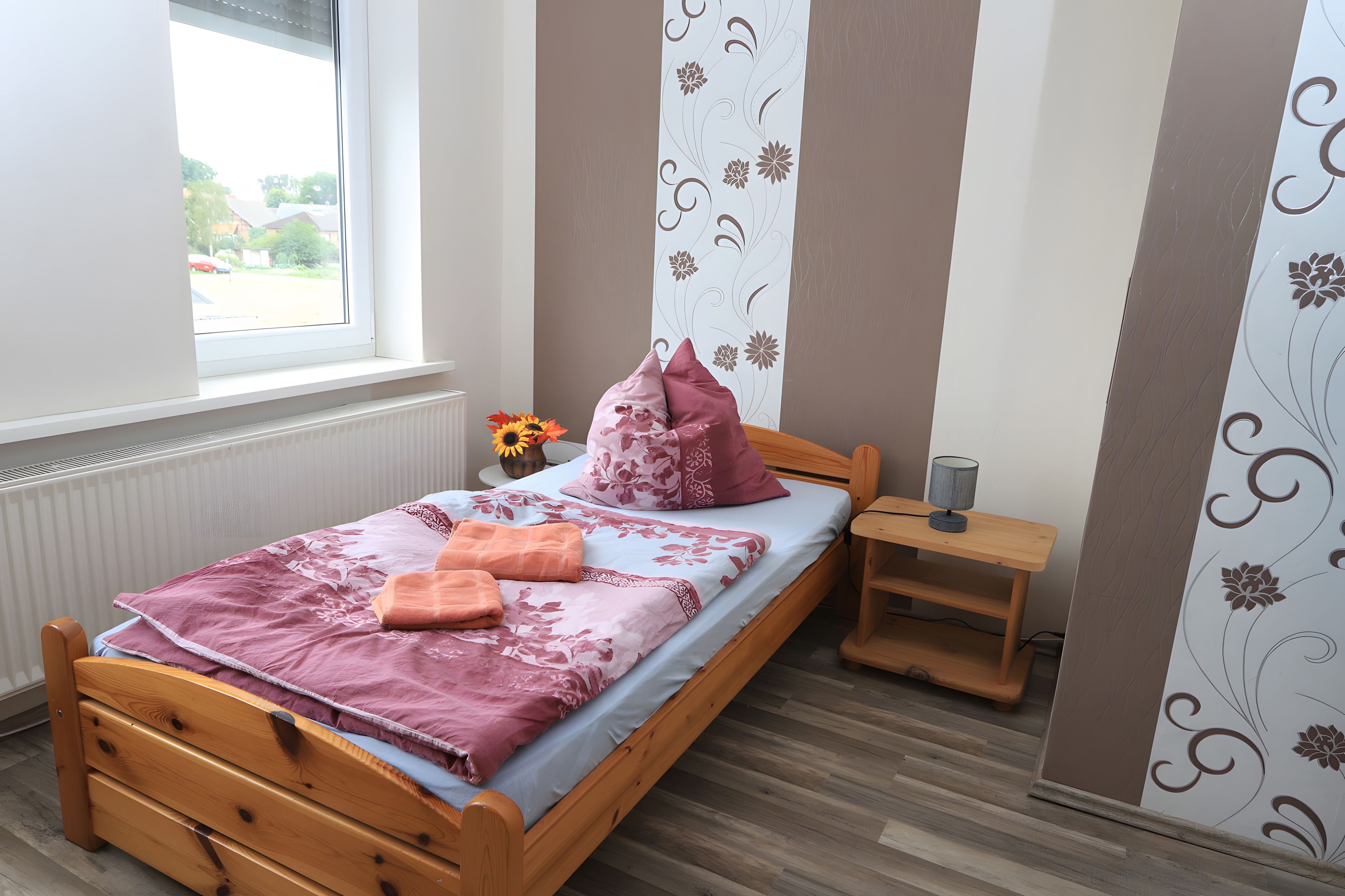 Quarto com cama de madeira, mesa de cabeceira, abajur e janela com vista para o exterior.