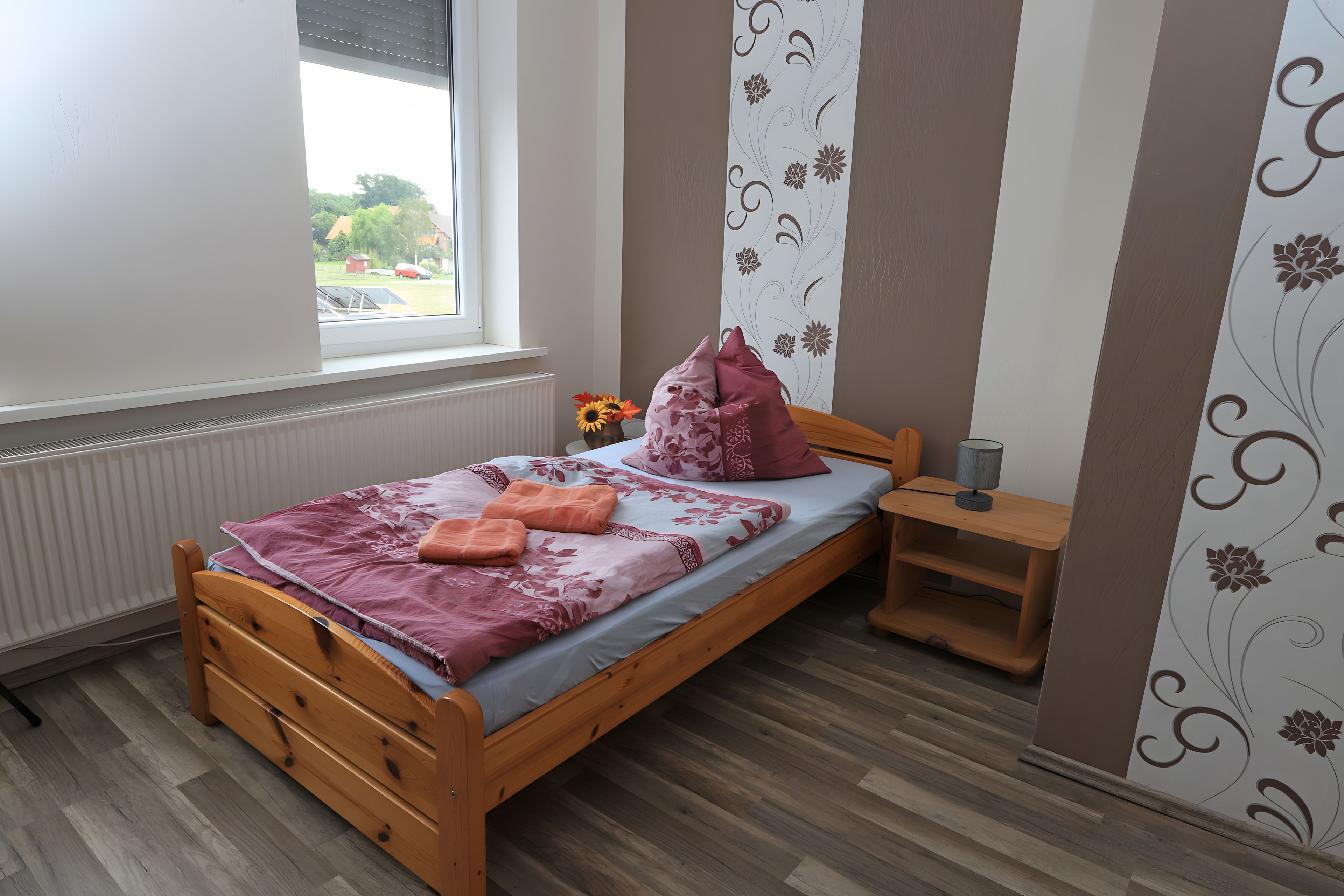A bedroom with a wooden bed, a nightstand, a window, and a radiator.