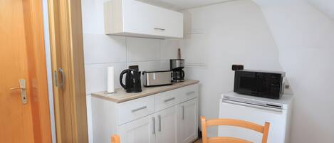 Una cocina compacta con armarios blancos, microondas, cafetera y tostadora.