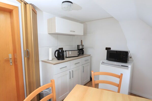 A compact kitchen with white cabinets, a microwave, a coffee maker, and a toaster.