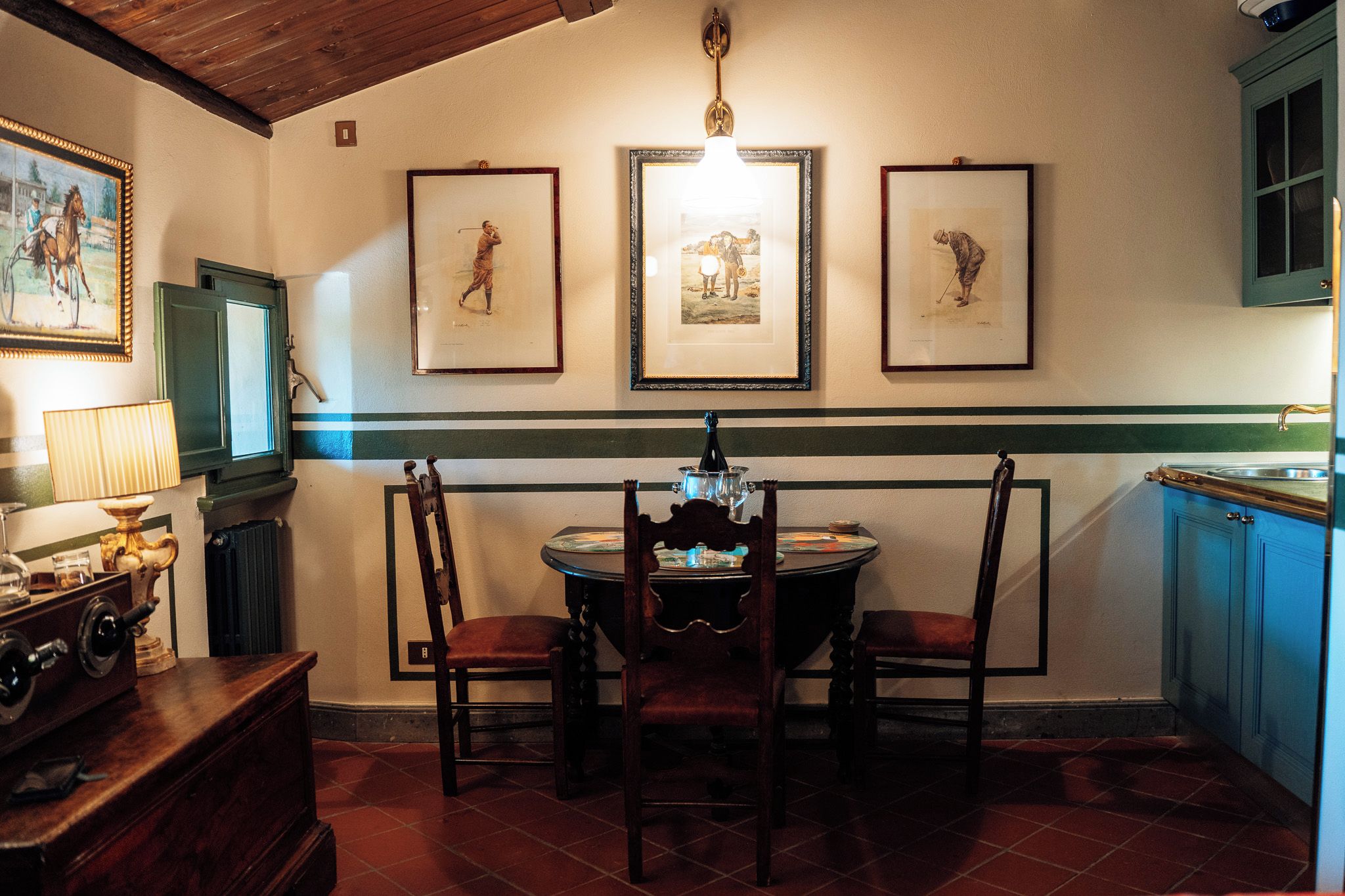 Een eetruimte met een ronde tafel, stoelen, een kroonluchter, ingelijste foto's aan de muur en een raam met uitzicht.