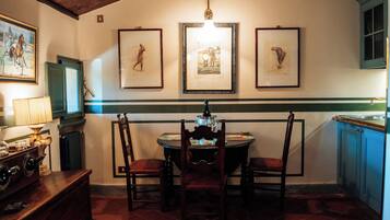 Een eetruimte met een ronde tafel, stoelen, een kroonluchter, ingelijste foto's aan de muur en een raam met uitzicht.