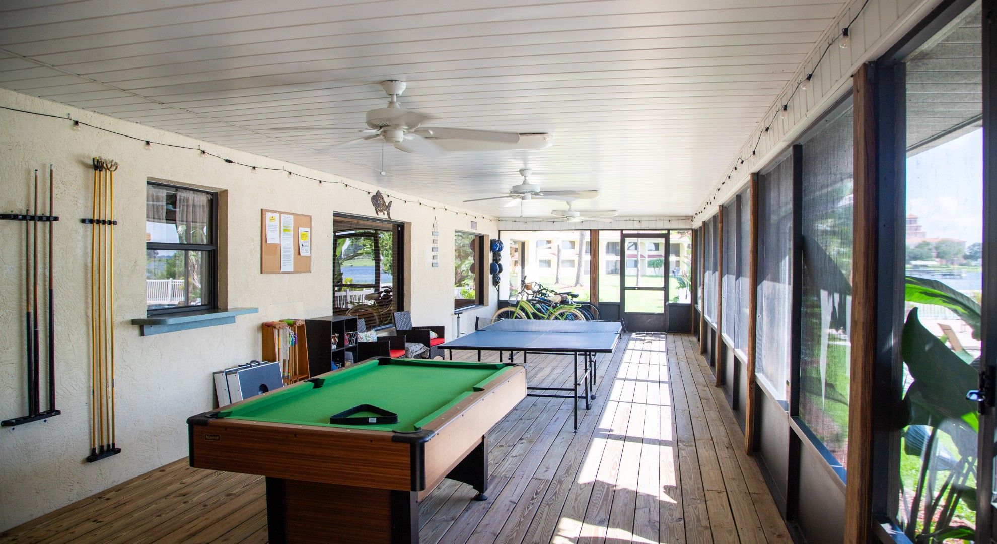 A pool table and billiards in a room with a wooden floor and ceiling fans.