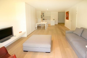 A modern living room with a flat-screen TV, a grey sofa, and a dining area with a table and chairs. - Apartment in Cadzand with swimming pool (Cadzand)