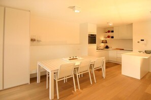 A compact kitchen with white cabinetry, a dining table with chairs, and a small island with a lamp. - Apartment in Cadzand with swimming pool (Cadzand)