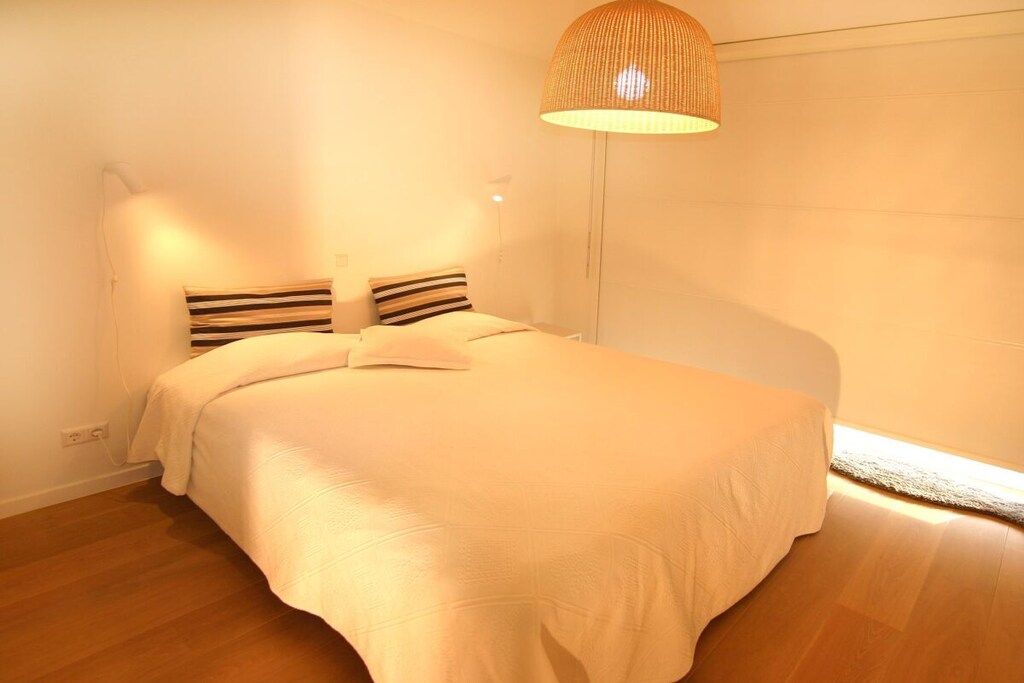 Een slaapkamer met een bed, twee kussens, een bedlampje en een hanglamp.