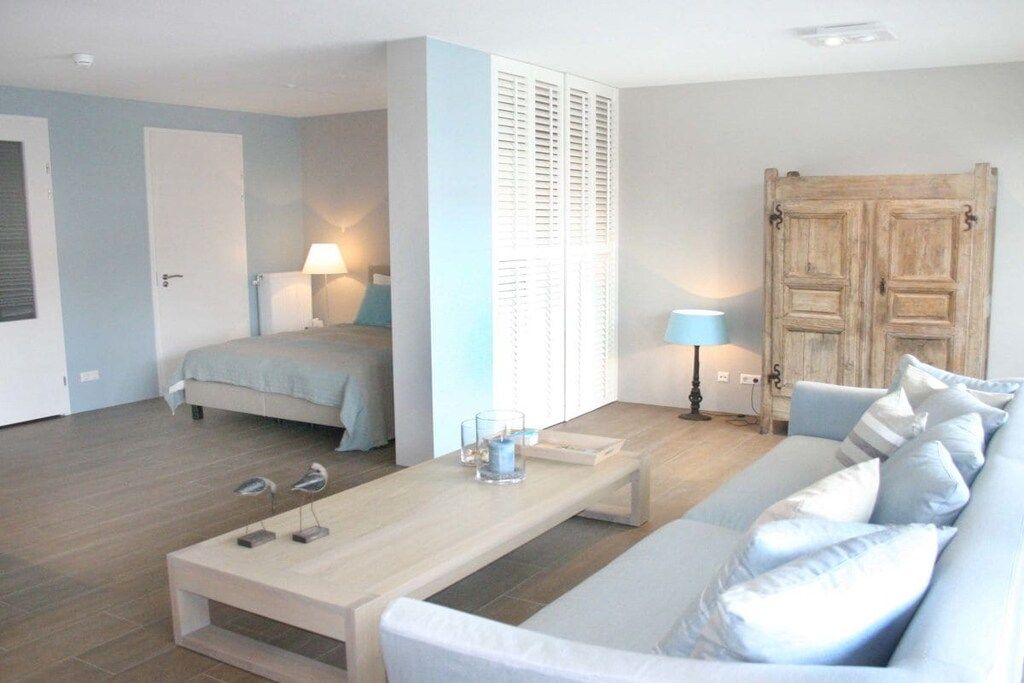 Een moderne slaapkamer met een bed, nachtkastje, lamp en een groot raam met luiken.