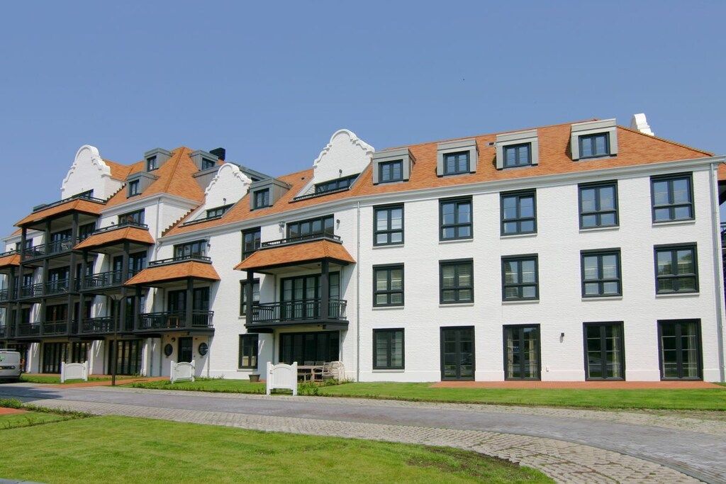 A multi-story residential building with balconies, a paved driveway, and a well-maintained lawn.