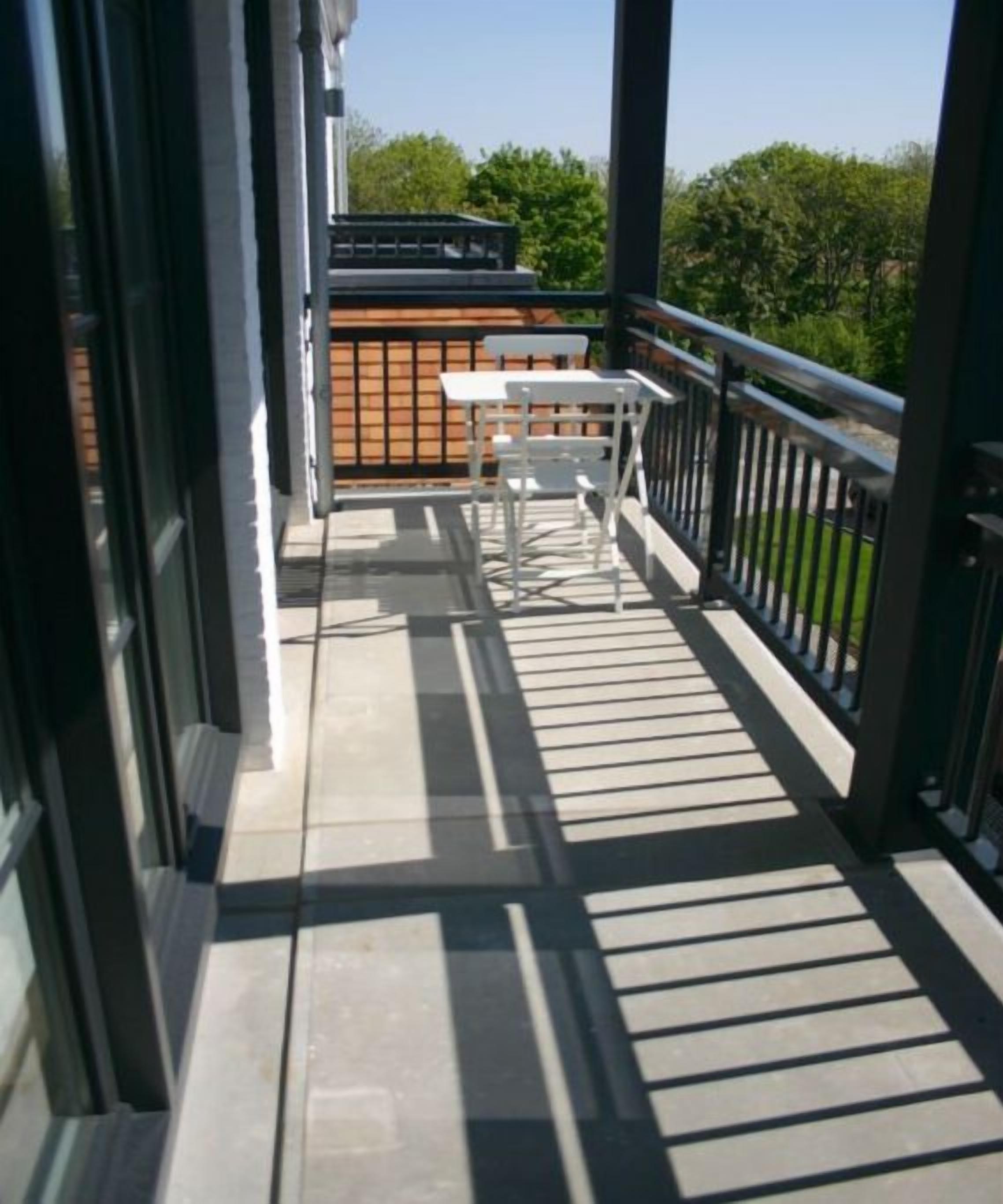 Un balcon avec une table et des chaises, une clôture en bois et une vue sur les arbres.