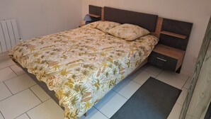 Quarto com cama, mesa de cabeceira, abajur e radiador.