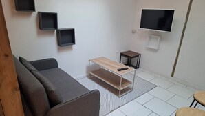 Uma sala de estar moderna com um sofá cinza, uma mesa de centro de madeira, uma pequena mesa lateral, uma TV fixada na parede e um tapete estampado.
