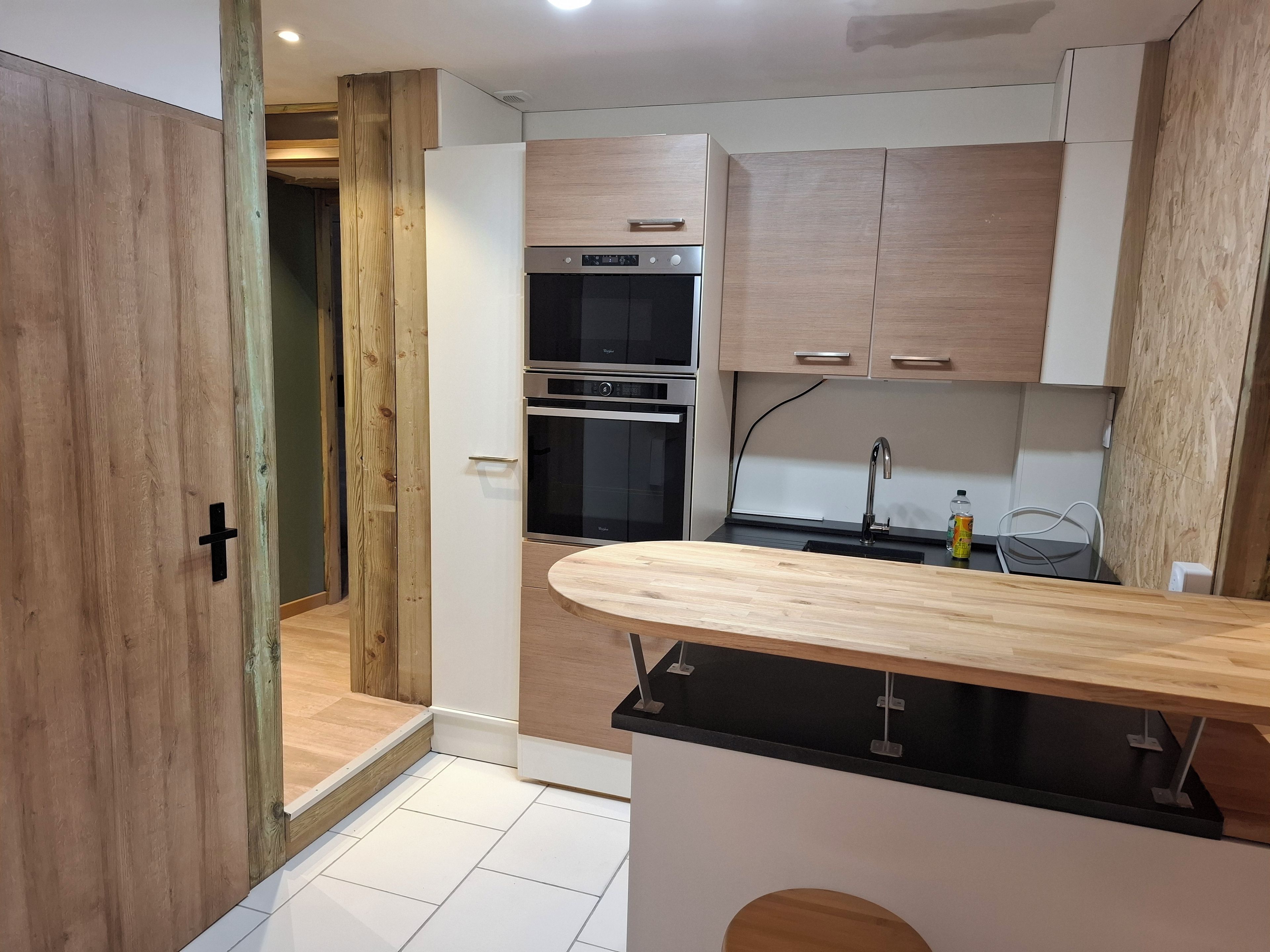 Une cuisine moderne avec des meubles en bois, un four encastré et un plan de travail noir.