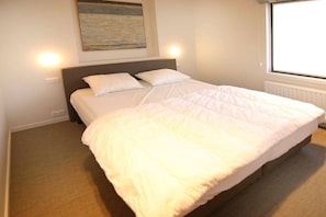 A bed with white bedding, a headboard, and a wall-mounted light fixture. - Holiday apartment with 1 bedroom (Cadzand-Bad)
