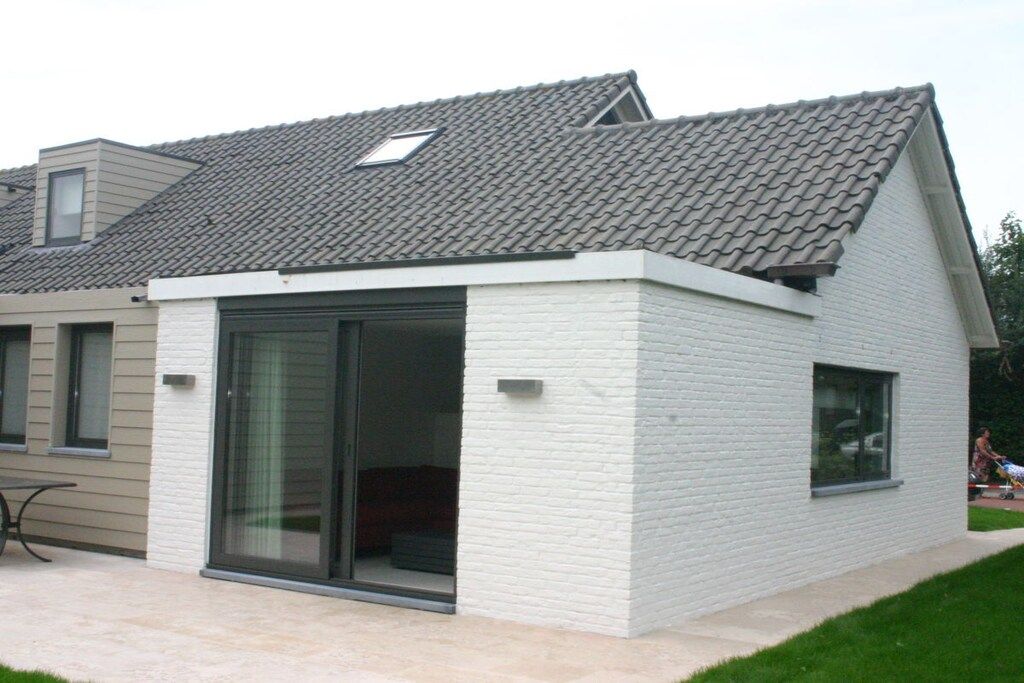 Une maison moderne avec un toit en pente, une grande porte-fenêtre coulissante et un petit garage attenant.