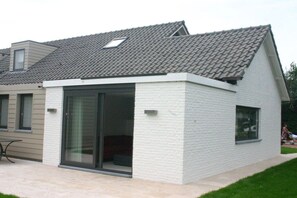 Une maison moderne avec un toit en pente, une grande porte-fenêtre coulissante et un petit garage attenant.