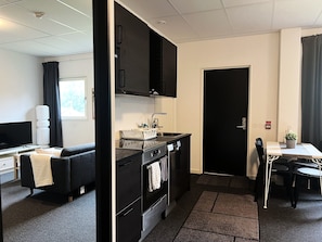 Una kitchenette compacta con estufa, pileta y alacenas, un pequeño comedor con mesa y sillas, y una zona de estar separada con sofá.