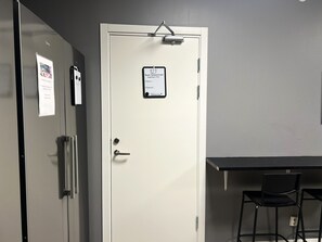 A door with a sign indicating a private bathroom and kitchen, a desk with a chair, and a wall-mounted light fixture.