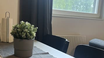 Una habitación con una mesa, sillas, una planta en maceta, un radiador y una ventana con vista a árboles.