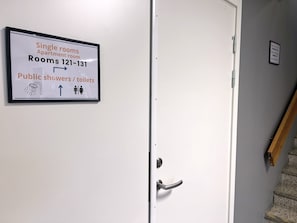Una puerta con un cartel que indica habitaciones individuales, habitaciones 121-131 y baños/inodoros públicos.