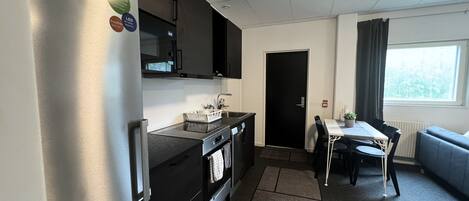 A compact kitchen with a refrigerator, stove, and sink. There's a dining area with a table and chairs, and a window with curtains.