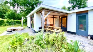 Una casa moderna con un portico coperto, un patio in legno e un giardino.