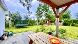 Un patio in legno con tavolo e candela, un trampolino e una piccola costruzione in legno in un giardino.
