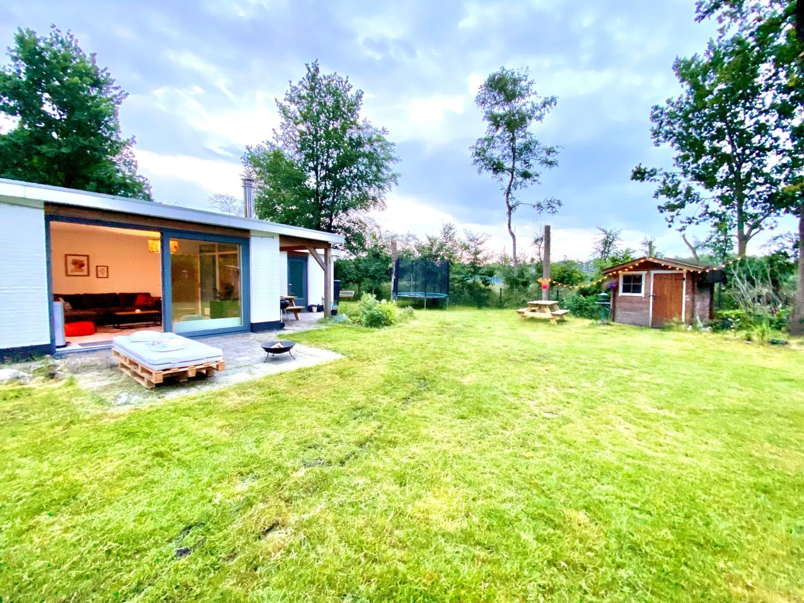 A modern house with a large glass door entrance, a patio area with a barbecue grill, and a small wooden shed in the backyard.