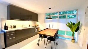 A modern kitchen with dark cabinets, a wooden dining table, and a large window with a view of greenery. - On the edge of the forest in Drenthe, with plenty of room for the whole family (Gasselte)
